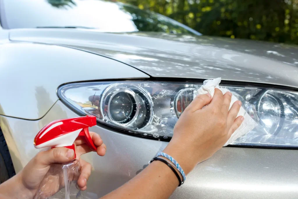Een man maakt de koplampen van een auto schoon.